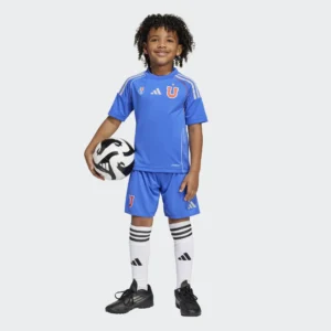 Minikit U. de Chile Local 2025 Adidas. Niño con uniforme de fútbol azul y balón. Equipación deportiva infantil.
